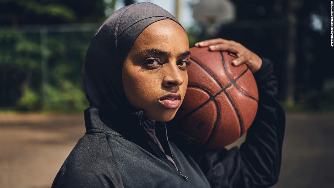 Moody portrait of basketball star Bilqis Abdul-Qaadir wearing Haute Hijab sports hijab for the "Can't Ban Us" marketing campaign, holding basketball on her shoulder.