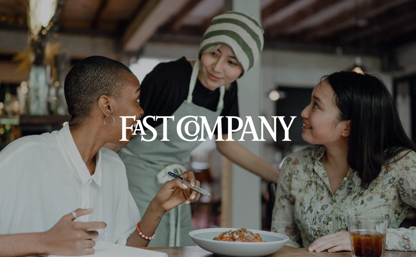 The Fast Company logo on top of an image of two people talking to a server at a restaurant